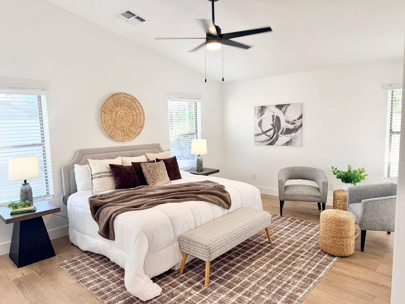 Primary bedroom staged with white bedding, a brown throw and woven wall decor in Gilbert, AZ
