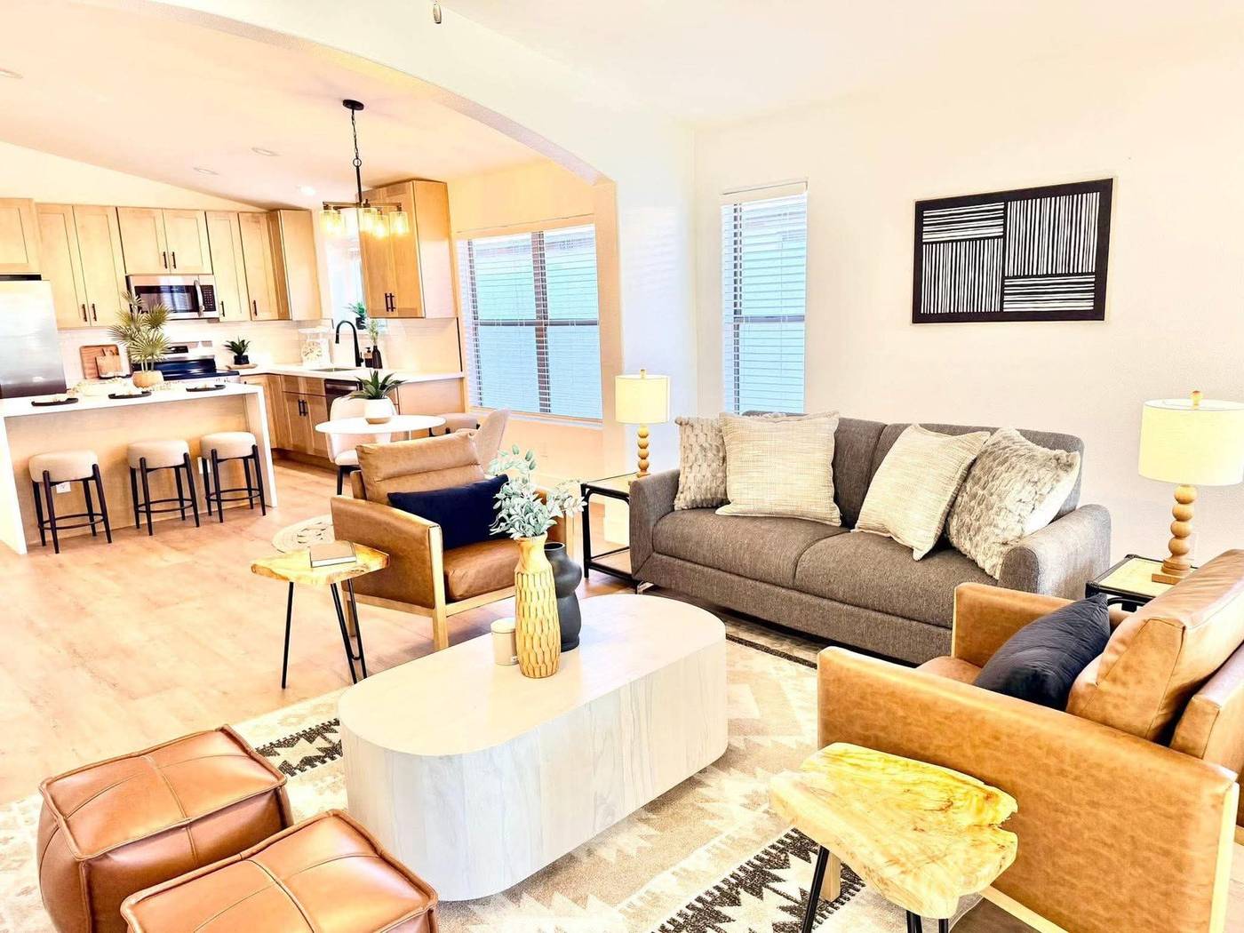 Living room staged with a leather ottoman, mustard accent chairs and a view into the kitchen