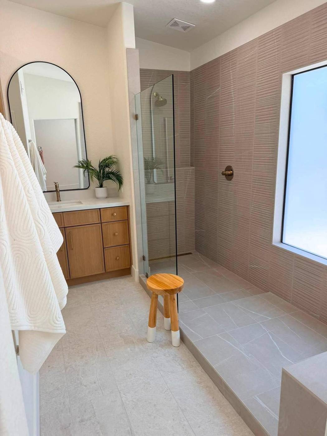 Bathroom staged with a walk-in shower, arched mirror and a wood stool