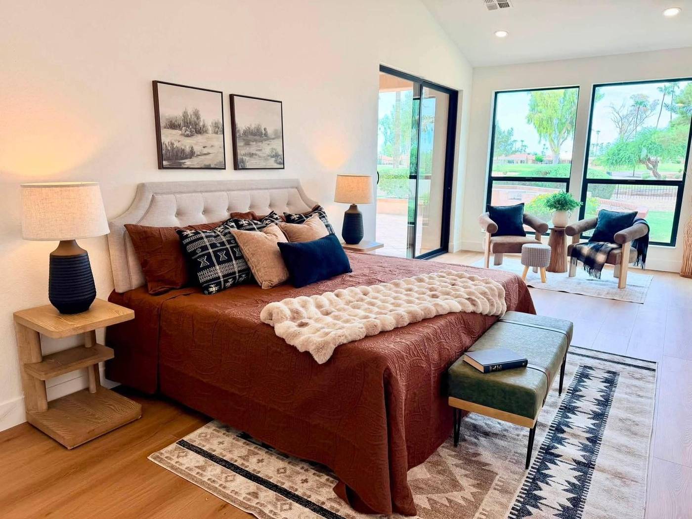 Primary bedroom staged with rust bedding, navy lamps and a window sitting area