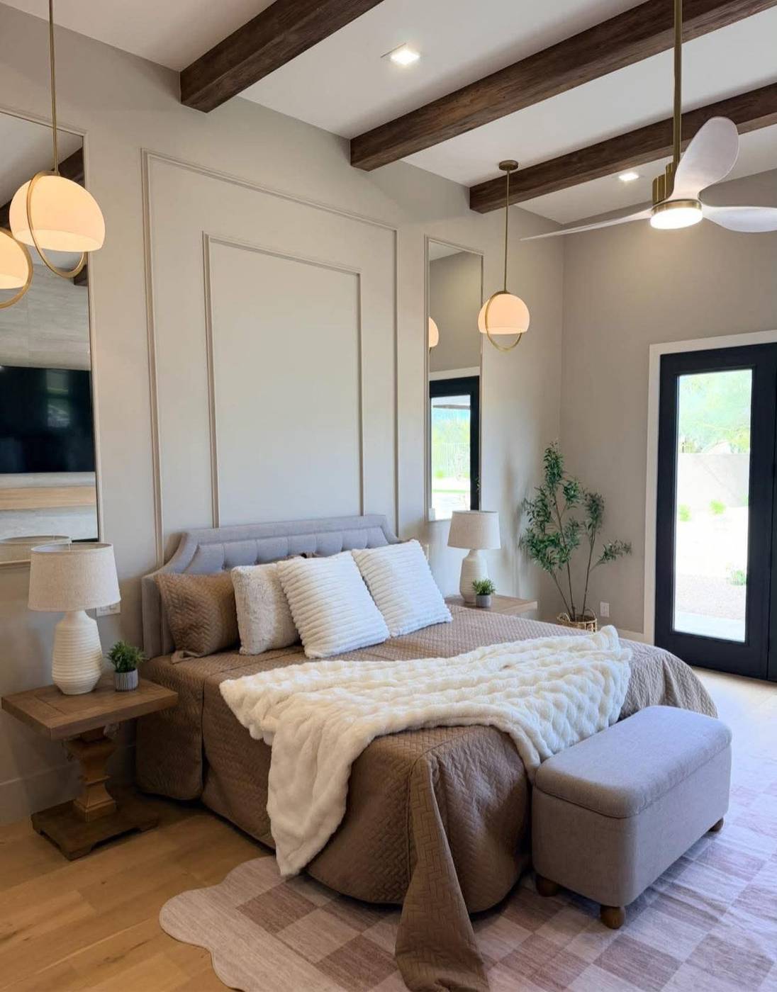 Primary bedroom with beamed ceiling staged in soft neutrals and a bench at the foot of the bed